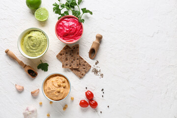 Bowls of different tasty hummus with crackers, lime and garlic on white background