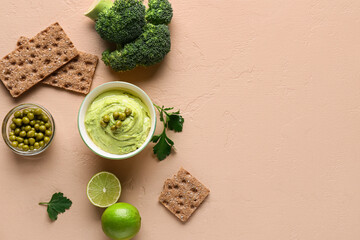 Bowl of tasty peas hummus with lime, broccoli and crackers on beige background