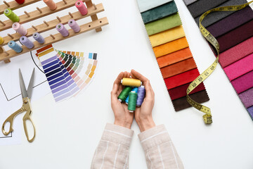 Female tailor holding thread spools and fabric samples at table in atelier