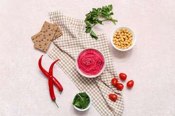 Bowl of tasty beet hummus with tomatoes, chilli peppers, parsley and crackers on pink background