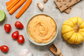 Bowl of tasty hummus with carrot, tomatoes, pumpkin and crackers on grey grunge background