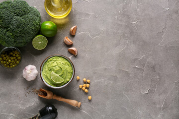 Bowl of tasty peas hummus with limes, broccoli and garlic on grey background