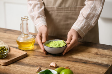 Woman with bowl of tasty peas hummus at table in kitchen