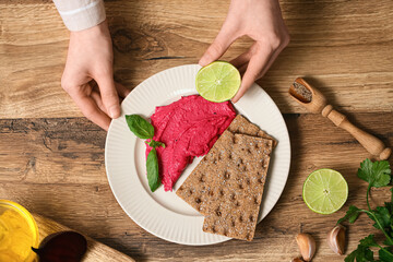 Woman squeezing lime onto tasty beet hummus on wooden background