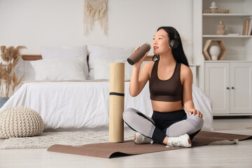 Sporty Asian woman with thermos and yoga mats at home