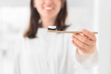 Woman with applied paste on bamboo tooth brush in bathroom, closeup