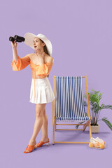 Obraz premium Surprised young woman looking through binoculars near deck chair on lilac background