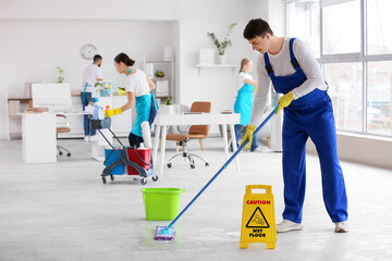 Male janitor mopping floor with his team in office