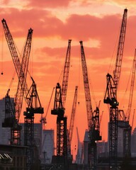 Dramatic Construction Cranes Silhouetted Against Fiery Sunset Sky
