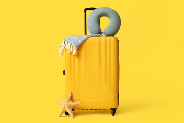 Obraz premium Stylish suitcase with travel pillow, towel and starfish on yellow background