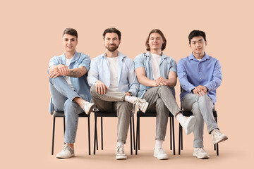Group of young men sitting on chairs against beige background