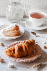 Crunchy and tasty french croissant on the plate over light wooden background. Breakfast with tea, sweet french dessert, pastry, close up