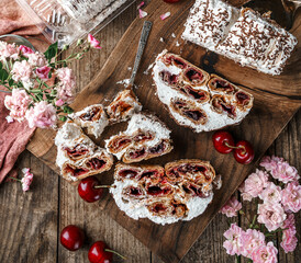 Monastic hut cake with cherry filling, cream and chocolate on wooden background with cup of tea and rose flowers. Holiday dessert, sweets and pastry, top view