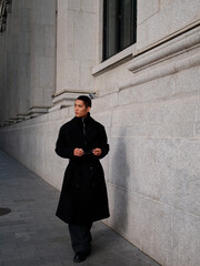 Portrait of handsome Chinese young man wearing black overcoat posing in the street, young guy with black short hair all in black with urban background. Male fashion, cool Asian young man lifestyle.