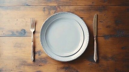 Empty white plates stacked on rustic wooden table with silver fork and knife arranged beside them suggesting a dining setting