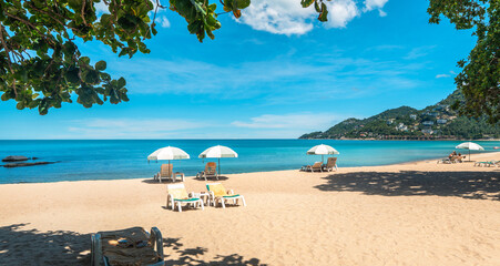 Tropical beach and sea with fresh summer sky on Koh Samui. Beach chairs and umbrellas. Seaside vacation. Summer getaway.