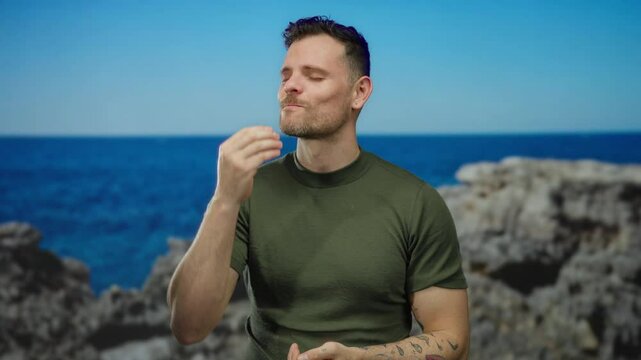 Man smiling at seaside with blue ocean background, wearing green shirt and showing thumbs up gesture, embodying confidence and leisure in a vibrant coastal setting.