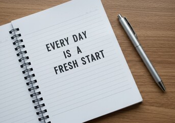 Open notebook with motivational quote and a silver pen on a wooden surface