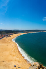 Aerial perspective of the sweeping golden coastline of Nazaré beach under clear sky