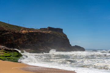Farol da Nazar&eacute; stands atop the cliff as powerful waves crash below