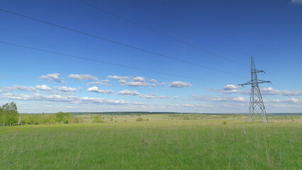 A vast, beautiful green field stretches out under a bright blue sky, where power lines run Time lapse.