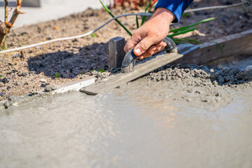 A man's hand is leveling freshly poured cement with a trowel, close-up