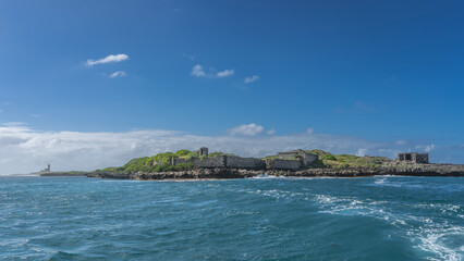 Obraz premium A small island in the ocean. The green hills and ruins of old buildings. Aquamarine water, blue sky with white clouds. Mauritius. Prison Island