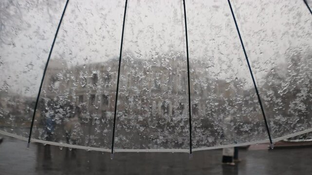 POV video, sleet falls on a transparent umbrella during a walk in the historical center of the European city, people go along the streets.