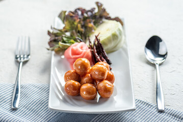 A plate of savory meatball appetizers with pickled ginger and chili peppers.