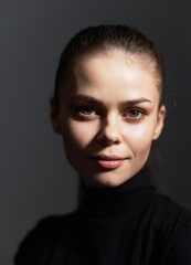 Obraz premium Young woman with a natural smile, wearing a black turtleneck sweater, portrait against a dark background, showcasing confidence and calmness.