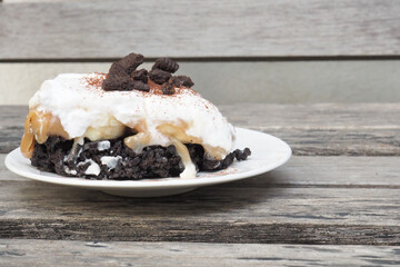 Delicious dessert with layers of cream, chocolate, and cookie crumbles, served on a rustic wooden table.
