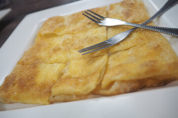 Delicious golden-brown pancake served on a white plate with two forks, perfect for a tasty breakfast or snack.