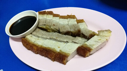 Deliciously crispy pork belly served with a rich dipping sauce on a pink plate.