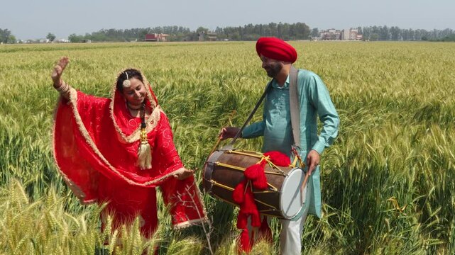 Punjabi sikh couple celebrating Baisakhi or vaisakhi festival in agriculture field and doing bhangra dance and play dhol. Culture of india. People of punjab.
