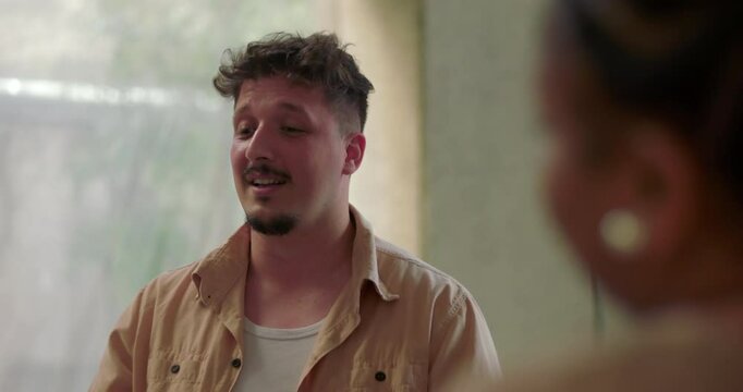 Man breaks down during group therapy, head lowered in emotional release as fellow group member offers silent support with a reassuring hand on shoulder