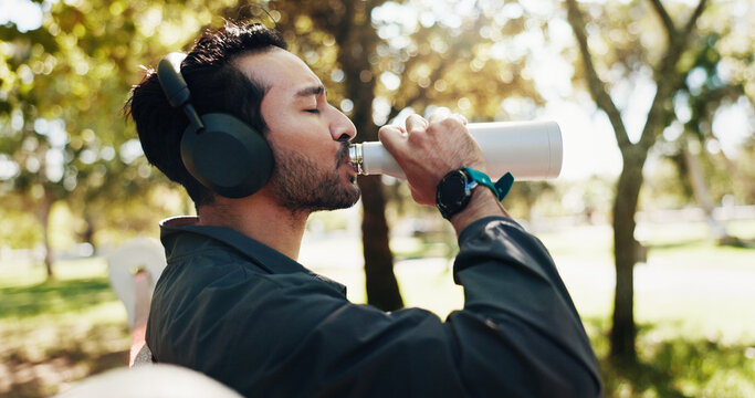 Break, drinking water and music with man in park for exercise, fitness or running routine. Headphones, hydration and streaming with athlete or runner outdoor in nature for recovery, relax and rest