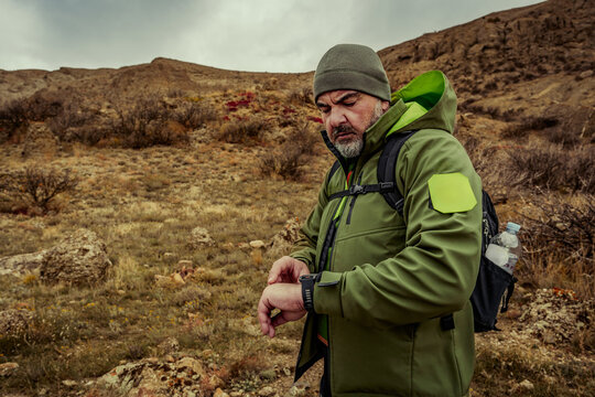 Man checks watch while hiking in rugged terrain during overcast weather in a mountainous area