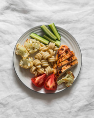 Delicious balanced lunch - grilled chicken breast, pasta, baked cauliflower, fresh vegetables on a light background, top view