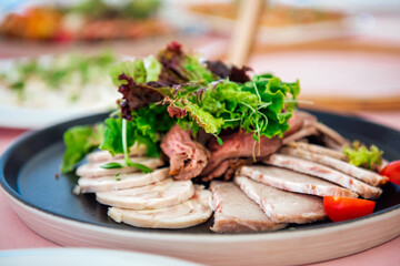 A plate with a variety of meat delicacies, decorated with lettuce leaves and microgreens. Meatloaf, roast beef, sausage. Snacks on the festive table at the event