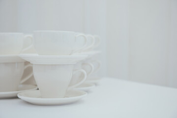 Lots of empty tea or coffee cups on a white table against a white wall, space for text.  Organization of events, catering, catering, beautiful white and gray background