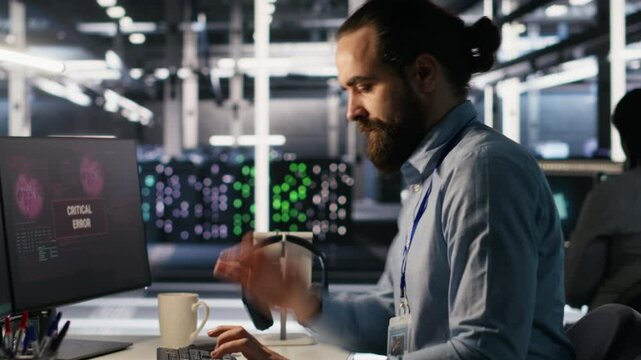 Engineer in data center frustrated by critical error popup on monitor during diagnostics session. IT expert stressed while troubleshooting system fault affecting infrastructure performance, camera A