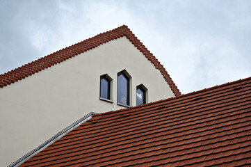 sloped brown clay tile shingle roof with white stucco gable end and decorative glass windows. ridge with dome shaped tiles. Zink metal flashing. detail of modern residential architecture