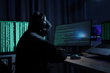 A man in a dark hoodie uses a laptop at night, symbolizing cybercrime, hacking, identity theft, and...
