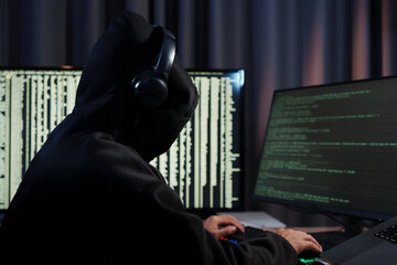A man in a dark hoodie uses a laptop at night, symbolizing cybercrime, hacking, identity theft, and...