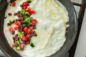 A top down view of an egg white omelet cooking in a non-stick pan, on the stove.