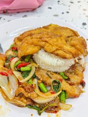Authentic Thai holy basil stir-fry with crispy pork belly (Moo Krob) and a fried egg (Kai Dao) over jasmine rice, a classic spicy and flavorful Thai dish.