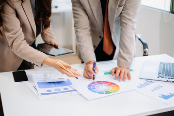 wo professionals collaborating on color schemes and marketing strategy using a color wheel and printed analytics.