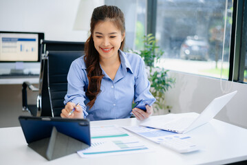 Asian woman in office working on business reports using laptop and documents. Perfect for finance,...
