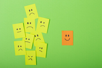 Positive attitude concept with Colorful Post-Its on Green Surface multiple faces and one standing out with a smile.