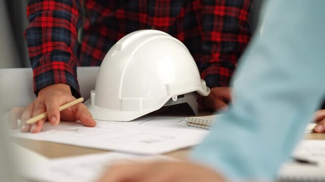 Architect and safety engineer discussion about building blueprint displaying on laptop on table with architectural document and wooden block scatter around at modern office. Closeup. Delineation.